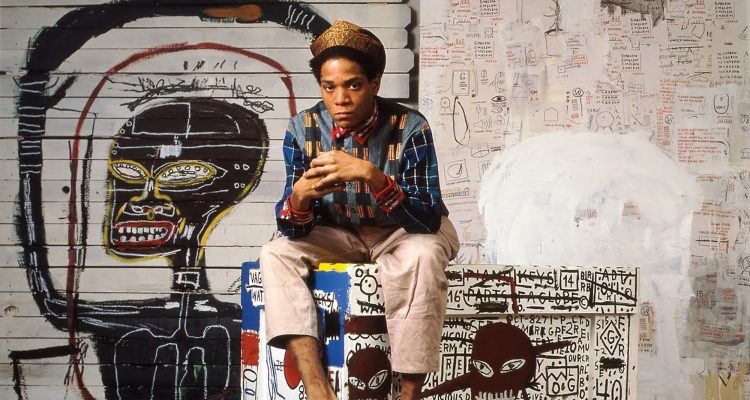 Basquiat poses for a photo in front of some of art work.